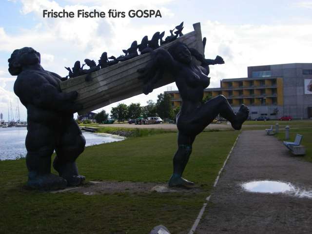 Die Skulptur "Frische Fische fürs GOSPA" zeigt zwei massive Figuren, die ein Boot mit Fischen tragen.