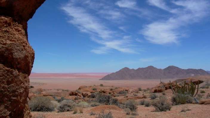 Eine Wüste mit Bergen im Hintergrund und einem blauen Himmel mit Wolken