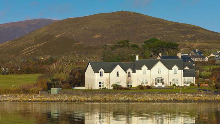 Ein großes weißes Haus steht in der Nähe eines Sees mit einem Berg im Hintergrund