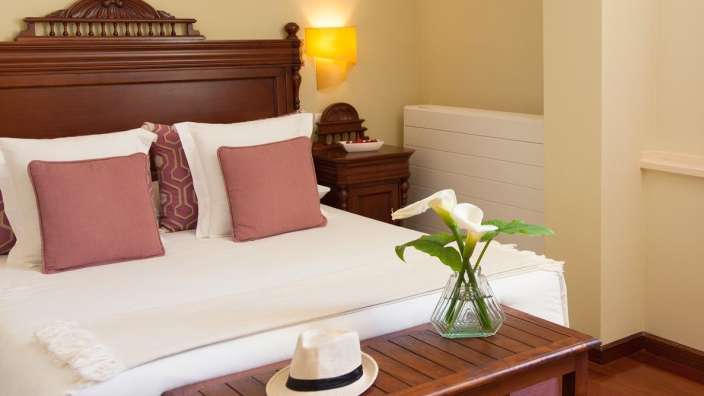 Ein Bett mit rosa Kissen und einem Hut auf einem Holztisch
