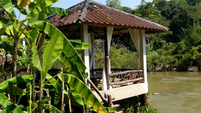 Ein kleines Gebäude mit einem braunen Dach sitzt am Ufer eines Flusses