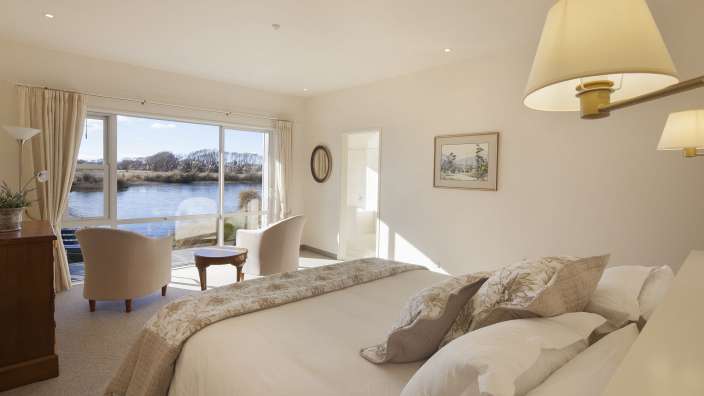Ein Schlafzimmer mit einem Bett und zwei Stühlen mit Blick auf einen Fluss