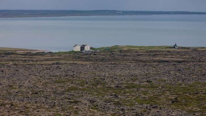 Ein kleines weißes Haus steht auf einem felsigen Hügel in der Nähe eines Sees