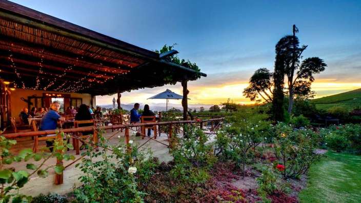 Eine Gruppe von Menschen sitzt auf einer Terrasse mit einem Sonnenuntergang im Hintergrund