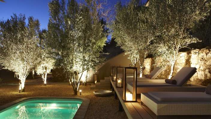 Ein Swimmingpool mit Liegestühlen und Bäumen beleuchtet
