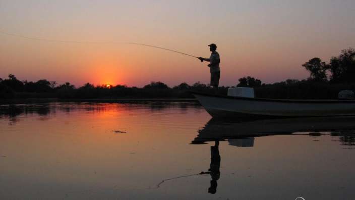 Ein Mann fischt bei Sonnenuntergang aus einem Boot