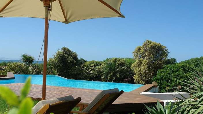 Ein Sonnenschirm steht auf einem Holzdeck neben einem Infinity-Pool
