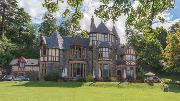 Ein großes Haus mit vielen Fenstern steht auf einem grünen Hügel