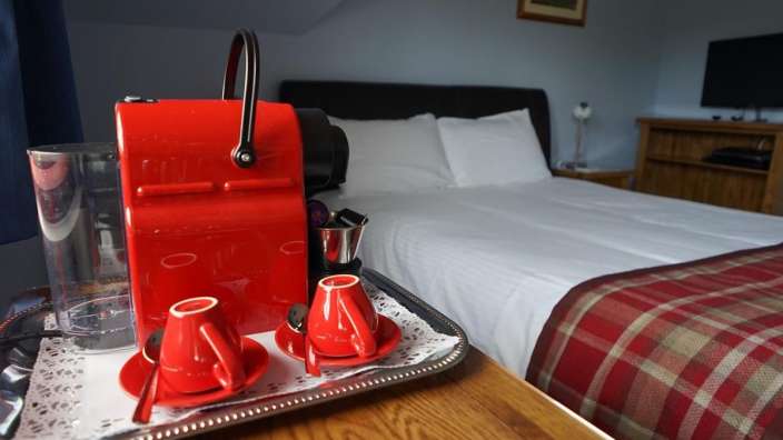 Eine rote Kaffeemaschine sitzt auf einem Tablett neben zwei Tassen Kaffee