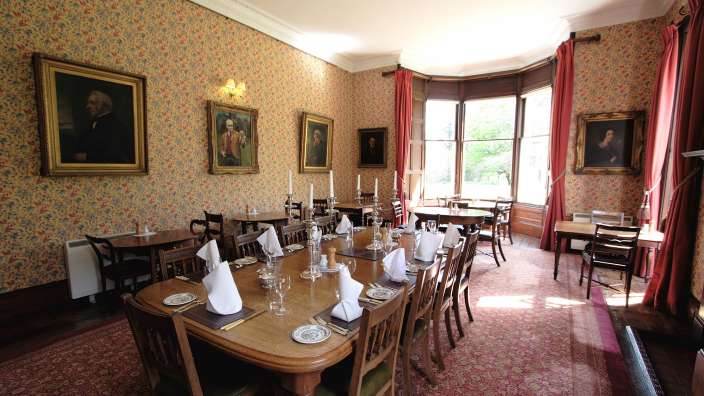 Ein Esszimmer mit Tischen und Stühlen und zwei Gemälden an den Wänden