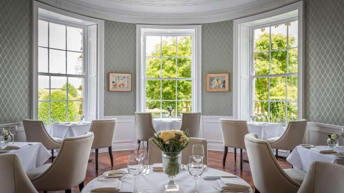 Ein Esszimmer mit weißen Tischen und Stühlen und vielen Fenstern