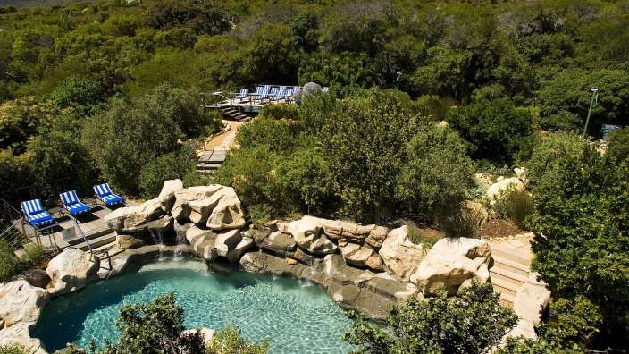 Ein großer Pool mit blauen Stühlen umgeben von Bäumen