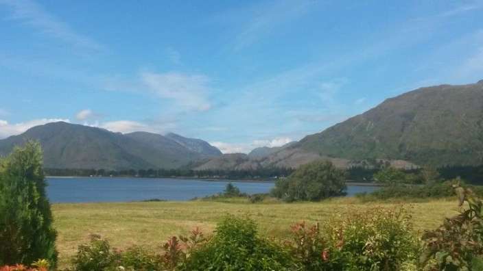 Ein See mit Bergen im Hintergrund und einem Feld im Vordergrund
