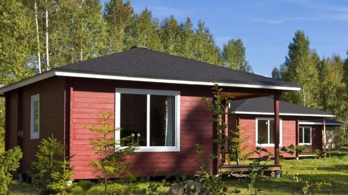 Ein rotes Holzhaus mit weißen Fenstern und einem schwarzen Dach