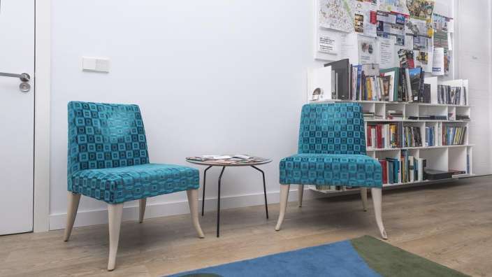 Zwei blaue Stühle stehen neben einem Tisch und einem Regal mit Büchern