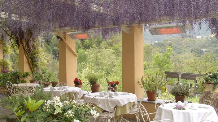 Eine Terrasse mit Tischen und Stühlen und lila Blumen