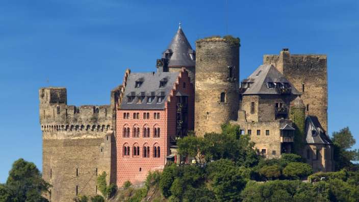 Ein altes Schloss auf einem Hügel mit einem roten Gebäude davor