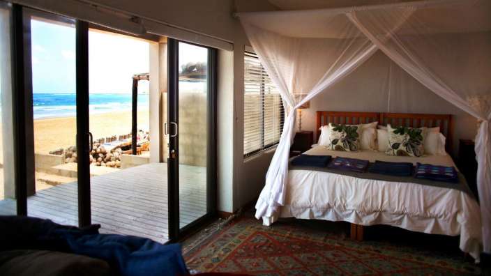 Ein Schlafzimmer mit einem Himmelbett und einer Glastür mit Blick auf den Strand