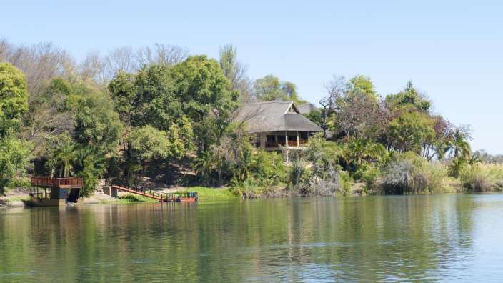 Ein Haus mit Strohdach sitzt auf einer kleinen Insel am Ufer eines Flusses