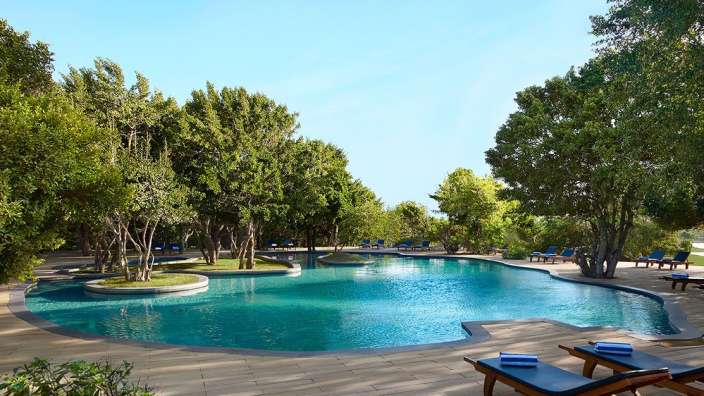 Ein großer Swimmingpool umgeben von Bäumen und Liegestühlen