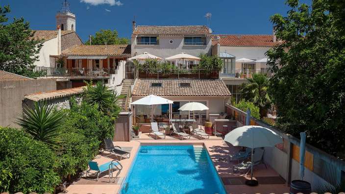 Ein großer Pool mit Liegestühlen und Sonnenschirmen in der Nähe eines Hauses