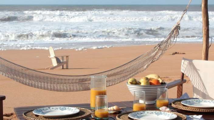 Ein Tisch mit Tellern und Gläsern auf einem Strand mit einer Hängematte im Hintergrund