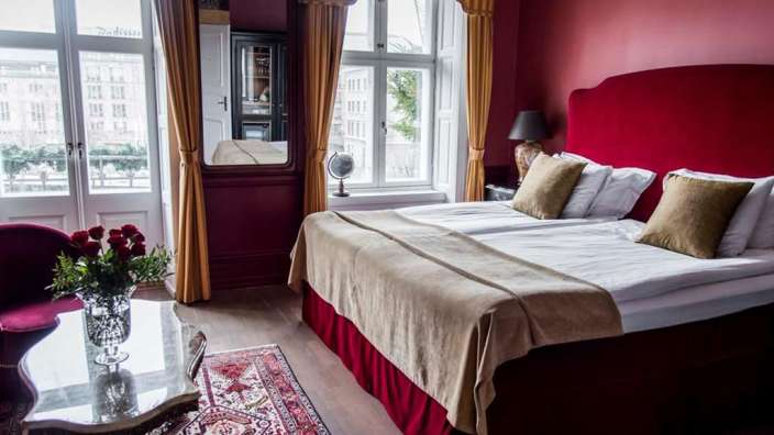 Ein luxuriös eingerichtetes Hotelzimmer mit einem großen Bett, roten Wänden und einem Fenster mit Blick auf die Stadt.