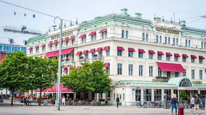 Eine Frau geht vor einem großen Hotel mit roten Vorhängen