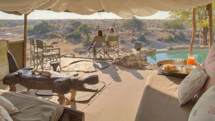 Zwei Personen sitzen auf einer Terrasse mit Blick auf einen Pool