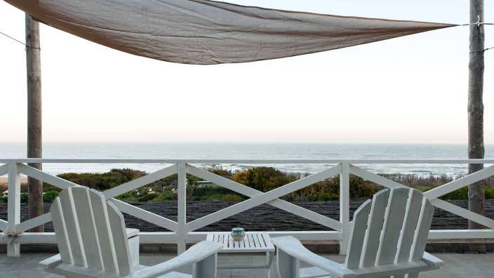 Zwei weiße adirondack-Stuhle sitzen auf einem Balkon mit Blick auf das Meer