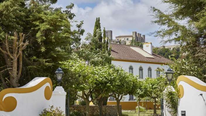 Ein weißes Haus mit einem braunen Dach steht inmitten von Bäumen