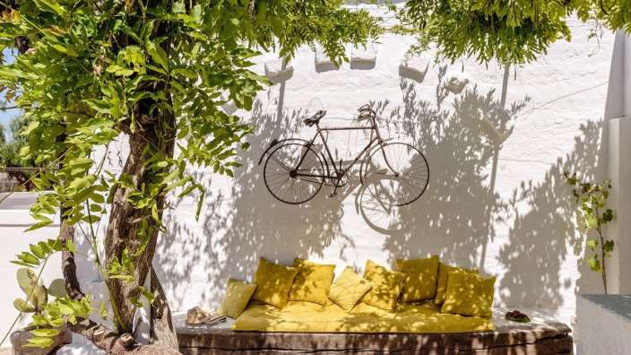 Ein Fahrrad hängt an einer weißen Wand neben einer Bank mit gelben Kissen
