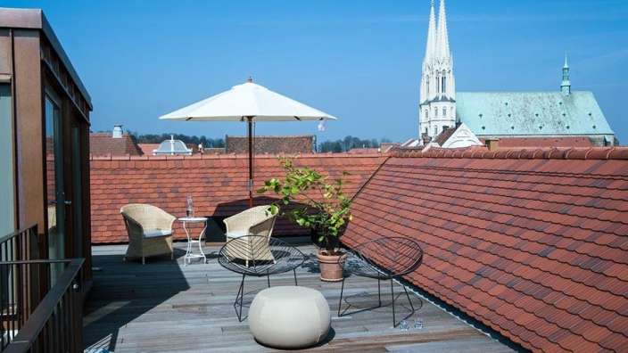 Ein Dachterrasse mit einem Tisch und Stühlen und einem weißen Regenschirm