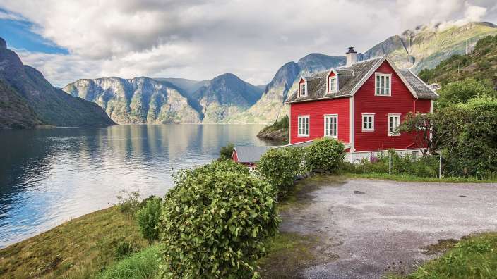 Ein rotes Haus steht an einem See mit Bergen im Hintergrund