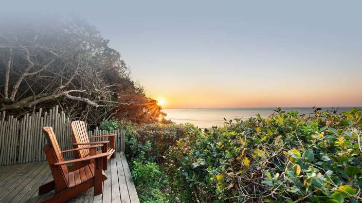 Zwei Holzstühle sitzen auf einem Holzdeck mit Blick auf das Meer