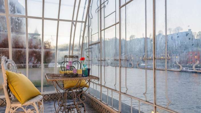 Ein Tisch und ein Stuhl in einem Glashaus mit Blick auf einen Fluss