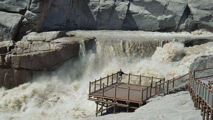 Ein Mann steht auf einem Holzdeck vor einem Wasserfall