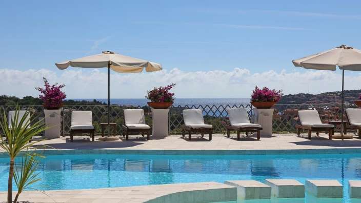 Liegestühle und Sonnenschirme um einen Pool mit Blick auf das Meer