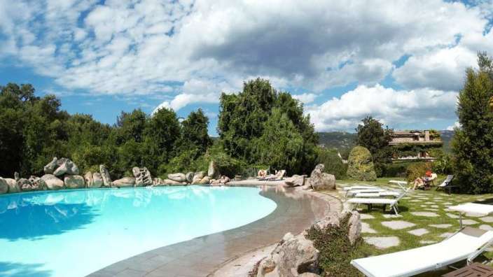 Ein großer Pool mit Liegestühlen und Bäumen im Hintergrund