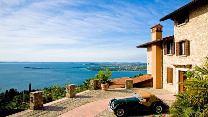 Ein Auto steht vor einem Steingebäude mit Blick auf einen See