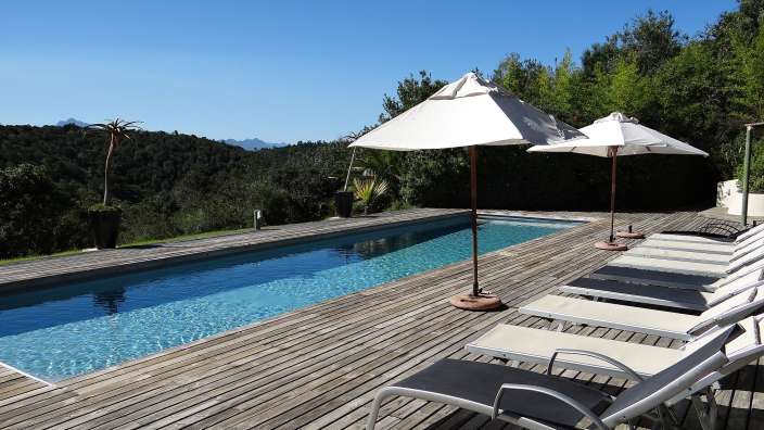 Liegestühle und Sonnenschirme stehen auf einem Holzdeck neben einem Swimmingpool