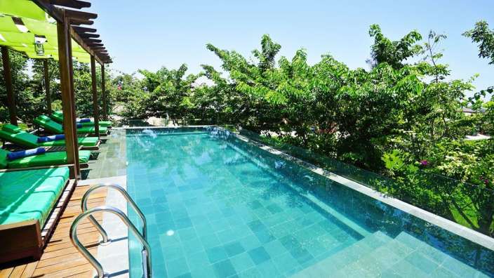 Ein großer Swimmingpool umgeben von grünen Stühlen und Bäumen