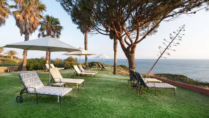 Liegestühle und Sonnenschirme auf einer Wiese mit Blick auf das Meer