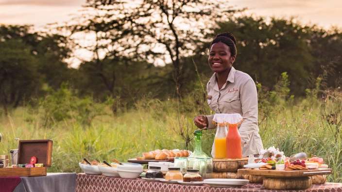 Eine Frau steht vor einem Tisch mit Essen und Getränken und lächelt