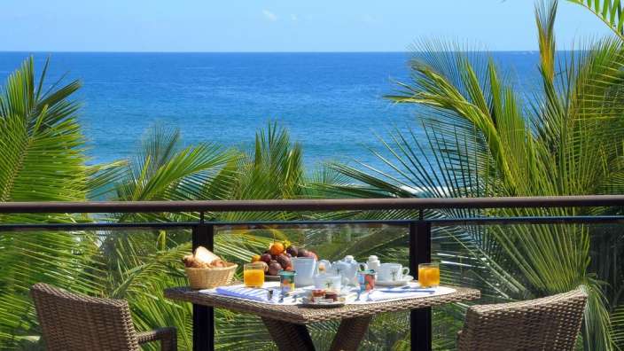 Ein Tisch mit einem Korb Obst darauf sitzt auf einem Balkon mit Blick auf das Meer