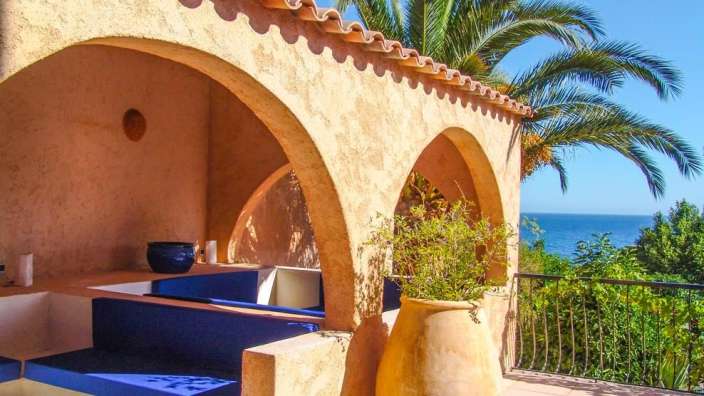 Ein Balkon mit blauen Bänken und einer Palme mit Blick auf das Meer