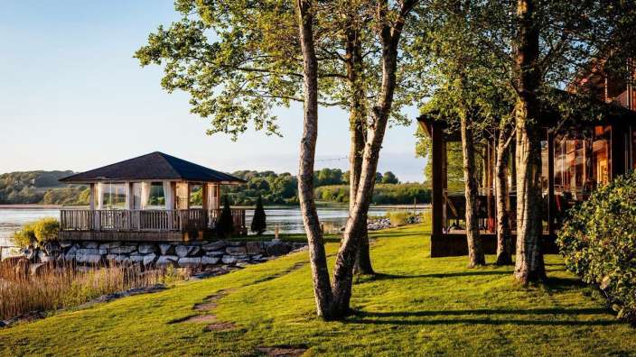 Ein kleines Holzgebäude mit einer Veranda steht am Ufer eines Sees