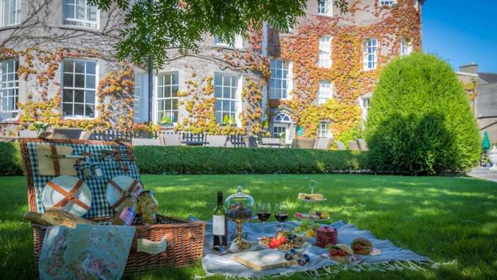 Ein Picknickkorb steht auf einer Decke im Gras vor einem großen Gebäude