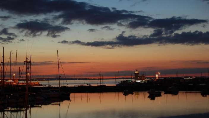 Sonnenuntergang in einem Hafen mit einem Leuchtturm im Hintergrund