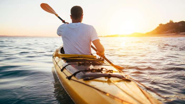 Ein Mann paddelt in einem gelben Kajak im Ozean